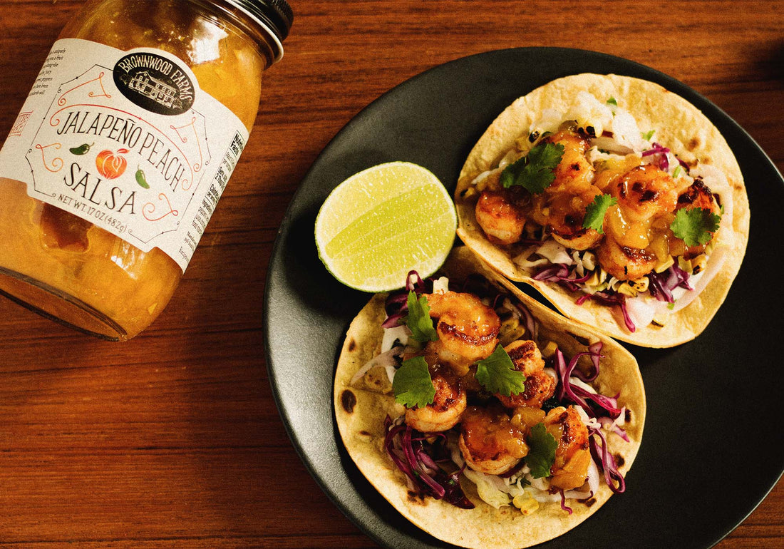 Easy, at-home shrimp tacos with Brownwood Farms Jalapeño Peach Salsa, shredded cabbage, and lime crema
