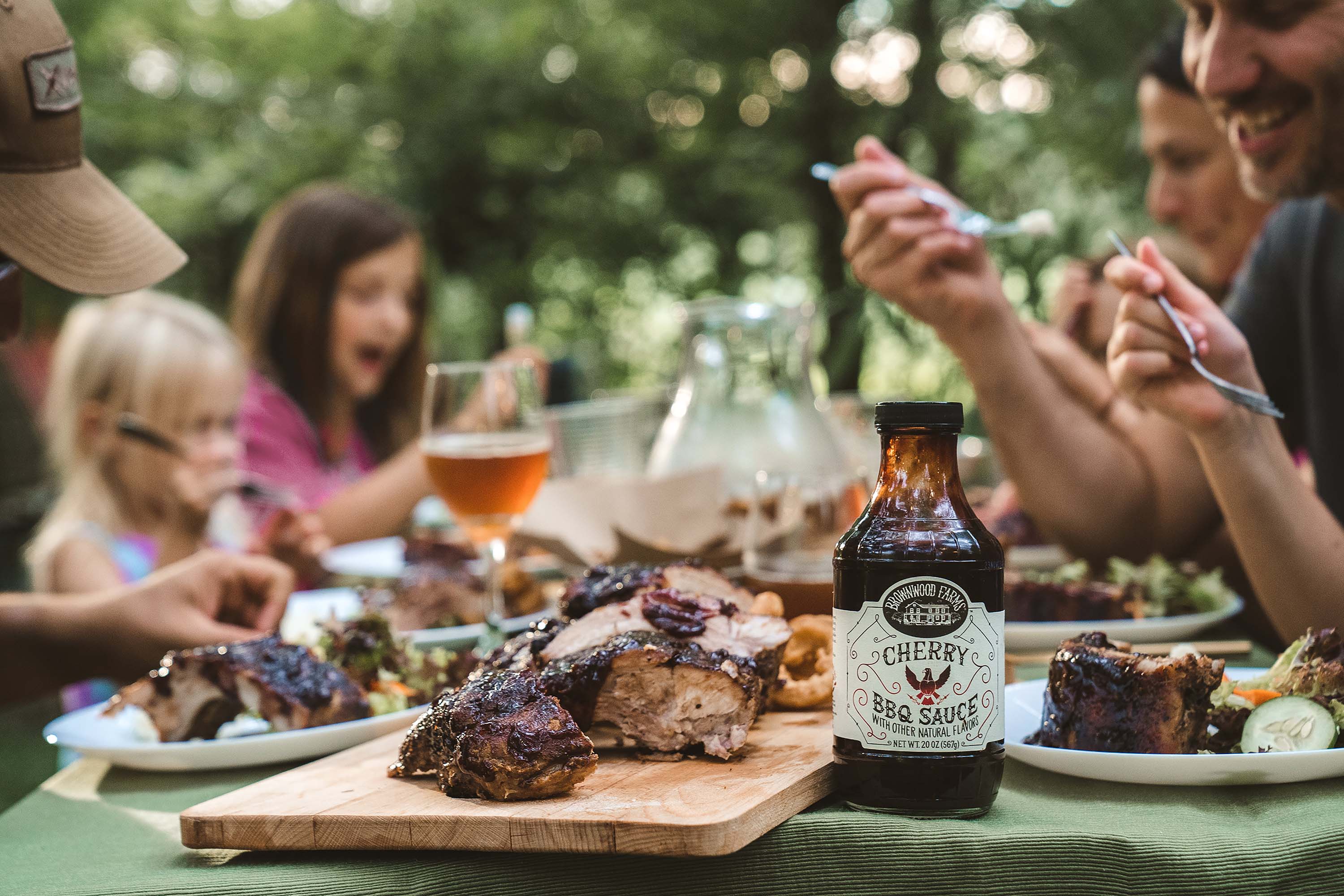 Family eating Brownwood Farms BBQ sauce on grilled ribs at a picnic table